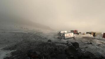 Top view of house high in mountains in blizzard. Clip. Cloudy weather with blizzard in mountains with houses and tourist attractions in winter. Winter storm in mountains at transit point with tourists video