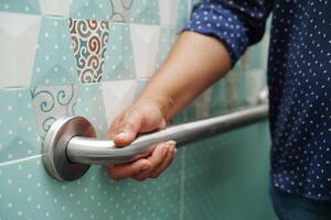 Asian woman use toilet support rail in bathroom, handrail safety grab bar, security in nursing hospital. photo