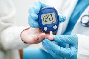 Asian doctor using digital glucose meter for check sample blood sugar level to treatment diabetes. photo