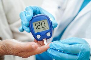 Asian doctor using digital glucose meter for check sample blood sugar level to treatment diabetes. photo