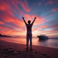 A man stands on the beach with his arms raised, looking out at the ocean photo