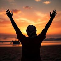 A man is standing on a beach with his hands raised in the air photo