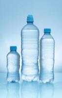 Three plastic bottles with frosted caps filled with water of different sizes on wet reflective blue surface photo