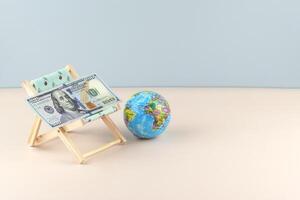 Chaise lounge with dollars and globe on a light background. photo