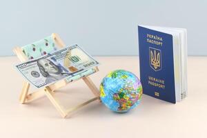 Ukraine passport and chaise lounge with dollars and globe on a light background. photo