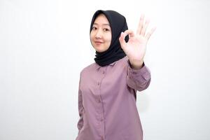 portrait of Indonesian Asian woman wearing shirt and hijab showing ok sign with one hand on eyes looking at camera through fingers. giving sign of agreement. Isolated on white Background photo