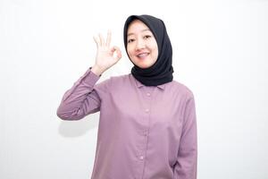 portrait of Indonesian Asian woman wearing shirt and hijab showing ok sign with one hand on eyes looking at camera through fingers. giving sign of agreement. Isolated on white Background photo