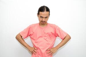 An Indonesian, Asian man wearing a pink tshirt shows a fierce expression as if he is angry or frustrated. isolated in white background photo