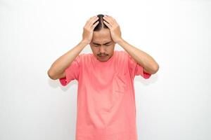 An Indonesian, Asian man wearing a pink tshirt having a headache, chest pain and stomach ache with hands holding head, chest and stomach. isolated in white background photo