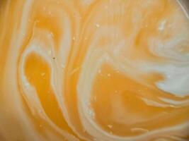High-angle full-frame shot of coffee and milk swirling together, featuring frothy foam bubbles and creating a captivating abstract pattern. photo