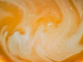 High-angle full-frame shot of coffee and milk swirling together, featuring frothy foam bubbles and creating a captivating abstract pattern. photo
