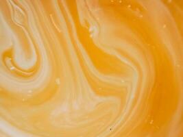 High-angle full-frame shot of coffee and milk swirling together, featuring frothy foam bubbles and creating a captivating abstract pattern. photo