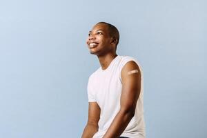 Young black man with a bandage on his arm happy to have been vaccinated against the corona virus. african american with injection bandage photo