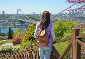 A young woman tourist with a backpack enjoys a panoramic view of the Fatih Sultan Mehmet Bridge. Back view.The photo was taken from Otagtepe