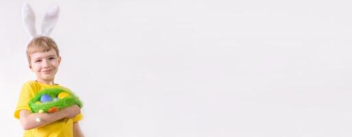 Happy Easter banner. Funny child boy in a white T-shirt in rabbit ears and with colorful Easter eggs on a white background with a place for text photo
