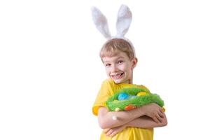 Happy child smiling in a yellow t-shirt in rabbit ears and with colorful eggs in a basket on a white background. Happy Easter concept with place for text. photo