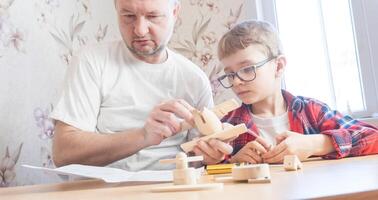 Happy father's day and childhood concept. Father and son-boy in glasses work with hand tools, using a screwdriver, assembling a wooden constructor at home at the table. photo