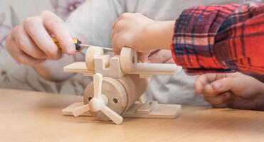 Happy father's day and childhood concept. Close-up of a father and a boy son in glasses work with hand tools, using a screwdriver, assembling a wooden house constructor at the table. photo