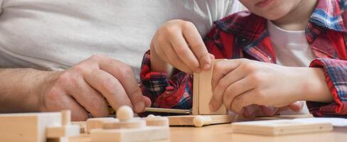 Happy father's day and childhood concept. Close-up of a father and a boy son in glasses work with hand tools, using a screwdriver, assembling a wooden house constructor at the table. photo
