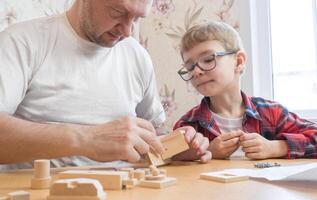 Happy father's day and childhood concept. Father and son-boy in glasses work with hand tools, using a screwdriver, assembling a wooden constructor at home at the table. photo