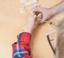 Happy father's day and childhood concept. Close-up of a father and a boy son in glasses work with hand tools, using a screwdriver, assembling a wooden house constructor at the table. photo