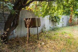 Rusty mailbox next to chain link fence. yard in background at an abandoned house photo