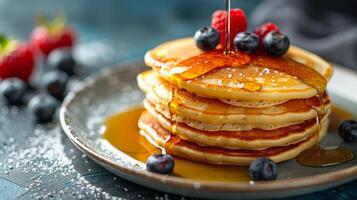 Fluffy pancakes stacked high, topped with berries and drizzled with maple syrup on a plate photo
