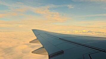 Airplane wing above clouds during golden hour, A serene view of an airplane wing slicing through clouds, captured during golden video
