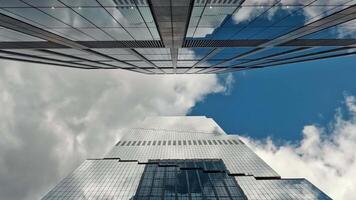 Upward view of modern skyscrapers against a cloudy sky Time lapse, A striking upward perspective of modern glass skyscrapers reaching into a partly cloudy sky, video