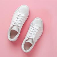 Stylish white sneakers on a pink background with shoelaces untied and a loose elastic band photo