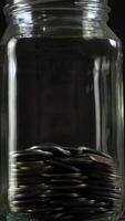 The jar overflows with neatly arranged coins, reflecting light beautifully. The dark background enhances the metallic sheen of the coins, creating an appealing visual contrast. video