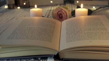 An inviting reading space features an open book resting on a table, flanked by glowing candles and a delicate rose, creating a warm atmosphere perfect for relaxation and reflection. video