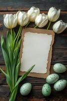 Decorative white tulips and speckled eggs arranged around a blank textured paper on a wooden table photo