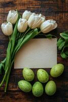 Decorative white tulips and speckled eggs arranged around a blank textured paper on a wooden table photo