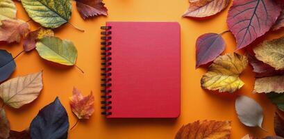 Autumn leaves surround a blank notebook on an orange background in a seasonal setting photo