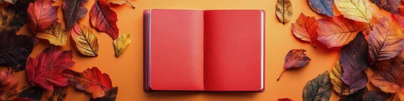 An open red book surrounded by colorful autumn leaves on a vibrant orange background photo