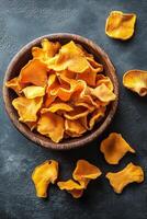 Brightly colored dried chanterelle mushrooms in a wooden bowl on a dark surface photo