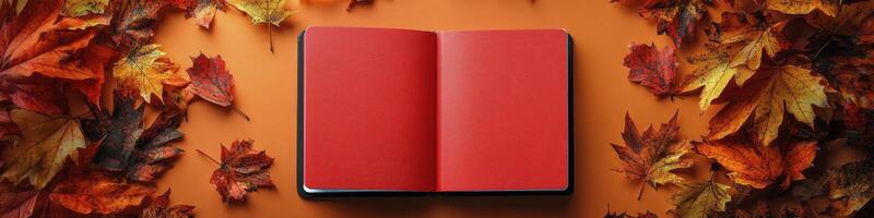 An open red book surrounded by colorful autumn leaves on a vibrant orange background photo