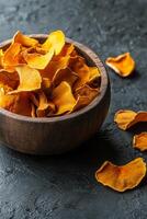 Brightly colored dried chanterelle mushrooms in a wooden bowl on a dark surface photo