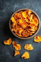 Brightly colored dried chanterelle mushrooms in a wooden bowl on a dark surface photo