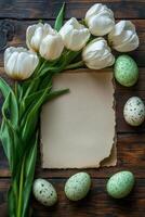 Decorative white tulips and speckled eggs arranged around a blank textured paper on a wooden table photo