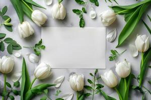 White tulips arranged around a blank card on a wooden table for personal messages and notes photo