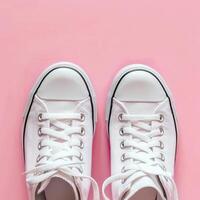 Stylish white sneakers on a pink background with shoelaces untied and a loose elastic band photo