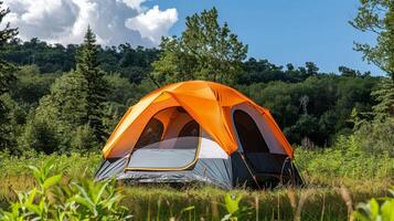 Bright orange tent set up in a lush green campsite under a sunny blue sky photo