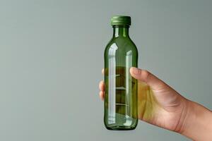 A hand holding a clear glass bottle against a subtle green background in soft lighting photo