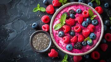 Colorful berry smoothie bowl topped with fresh fruits and mint leaves on a dark background photo