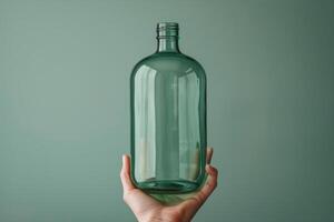 A hand holding a clear glass bottle against a subtle green background in soft lighting photo