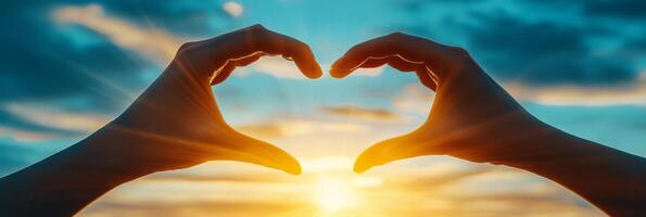 A hand forms a heart shape against the backdrop of a sunset over the ocean photo
