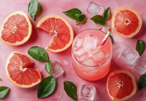 Slices of grapefruit arranged with ice cubes on a pink background for a refreshing drink idea photo