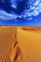 Expansive desert landscape with golden sand dunes under a bright blue sky and fluffy clouds photo